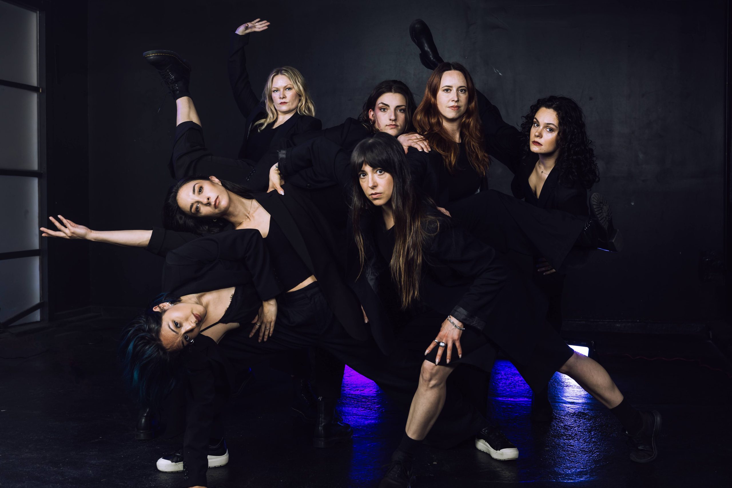 a group of black-clad dancers in a dynamic arrangement in a dark space